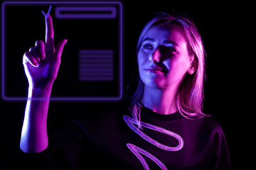 Beautiful blonde girl in pink-blue lighting presses a checkmark button on a virtual display with a neon purple hologram in the air