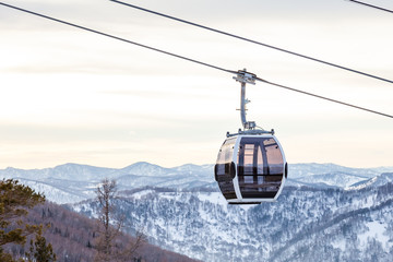 Cabin of a gondola cableway suspended on a rope where sits people with skis and snowboards high in the Altai mountains with snow and blue sky on winter sunset. Ski resorts and snowboarding. © Aleksandr Kondratov