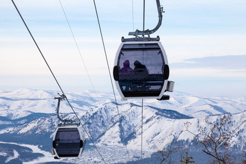 Cabin of a gondola cableway suspended on a rope where sits people with skis and snowboards high in the Altai mountains with snow and blue sky on winter sunset. Ski resorts and snowboarding. © Aleksandr Kondratov