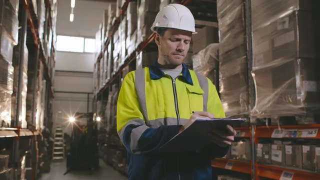 Portrait of young male manager checking stocks on clipboard in warehouse.