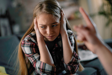 Mother scolding daughter. Scared girl covering ears . 
