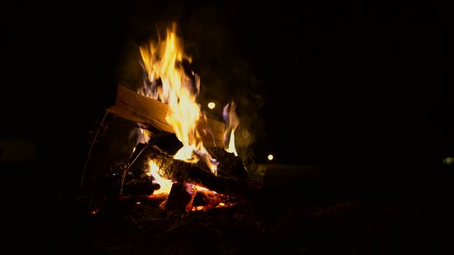 Static shot of a camp fire at night as a fresh log begins to burn on the fire.  4k 23.98fps.