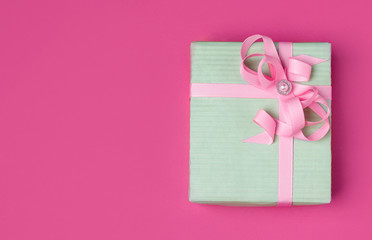 gift in a mint-colored wrapper with a pink ribbon on a pink background with copy space.