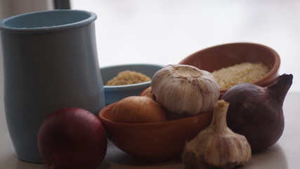 clay jugs, saucers with cereals, onions and garlic on the background of the window