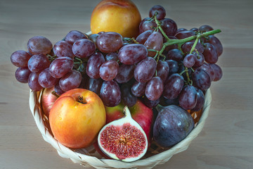 Naklejka na ściany i meble figs, nectarine and red grapes in a straw basket on a wooden background