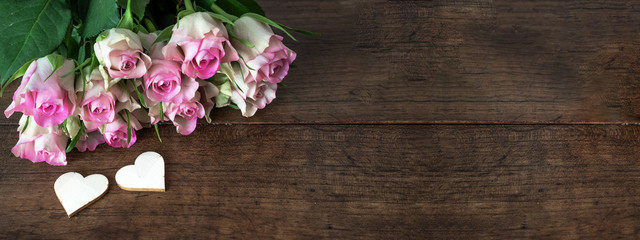 Fototapeta na wymiar pink roses on rustic wooden table and two wooden hearts, with space for text