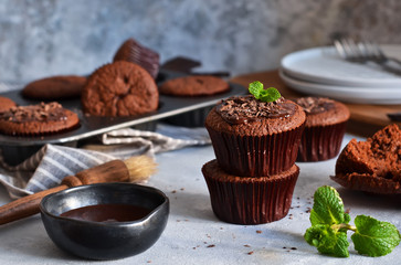 Chocolate muffins with chocolate moss sauce and mint on a concrete background.
