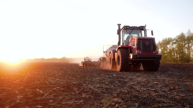 Rural seasonal works on farm land by industrial farming machinery or tractor on nature field at sunset. Agricultural cultivation for production organic food. Concept of farmland, agriculture equipment