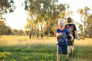 Fototapeta premium Little boys playing together in vibrant field at sunset with copy space