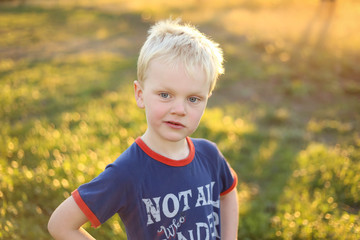 Little boy smiling and posing in a lush field at sunset. Vibrant image of blonde haired caucasion  child happy to be out in nature.