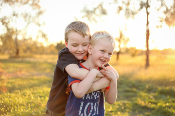 Little boy giving his little brother a piggy back. Boys playing together in vibrant field at sunset with copy space.