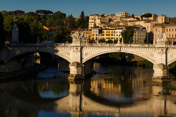 Fototapeta na wymiar The beautiful and majestic eternal city of Rome, the capital of Italy, in the early morning at sunrise from the bridge of San Angelo, the view of the bridge and the Tiber river and the dawn reflection
