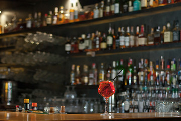 Red cocktail on bar counter. Drink with martini, gin, rum, tequila and fruit on the background of bottles with alcohol. Glass with booze on a wooden board.