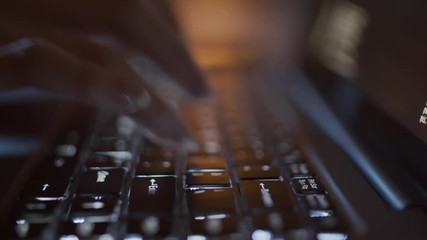 Close-up backlit shot of laptop, hands and fingers of unrecognizable woman typing on keyboard keys in darkness late at night, and lines of symbols moving on black screen