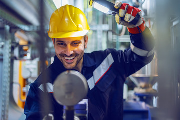Hardworking smiling blue collar worker in protective working suit and with helmet adjusting...