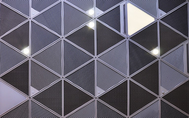 Texture of the system of suspended ceilings with metal profiles and metal mesh with built-in lights and spots. Gray ceiling with triangular cells