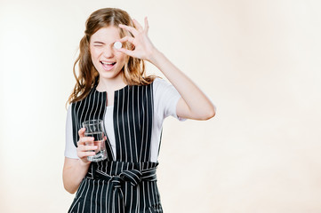 A young girl of about 20 holds a glass of water in her hands and shows the ok sign to her eye with vitamin. health concept.