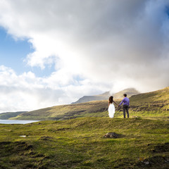 A happy couple in wedding dresses or the bride and groom holding hands and looking at the picturesque nature. Faroe Islands