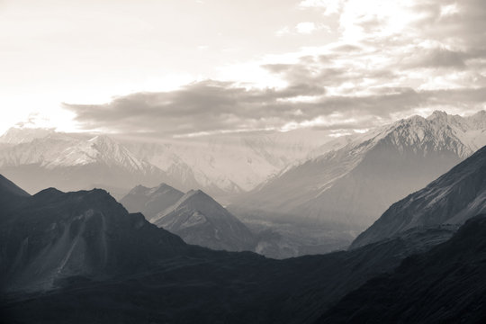 Nature aerial landscape view black and white photo of sunrise over snow capped Karakoram mountain range with morning fog in Nagar valley. Gilgit Baltistan, Pakistan.