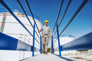 Young handsome caucasian businessman in suit and with helmet on head walking on bridge and looking...