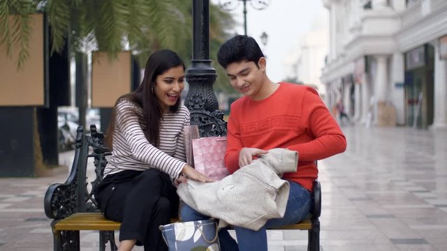 Young boyfriend girlfriend exchanging valentine's special gifts with each other. Cute Indian couple sitting on a bench in casual wear  giving presents to each other while celebrating valentine's da...