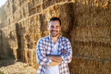 Handsome caucasian smiling farmer standing outdoors with arms crossed and looking at camera. In...