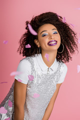 funny african american girl with dental braces, with silver glitter eyeshadows and purple lips wearing paillettes dress, isolated on pink with confetti