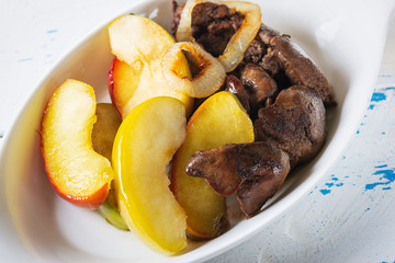 The chicken liver with the glazed apples and onions flamed in cognac on white plate. Old, wooden background. Close up. Selective focus.