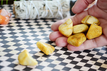 Woman's hand holding yellow jasper healing crystals. Tumbled yellow crystals, natural lighting and lush color. Intricate yellow swirls on beautiful jasper, witches healing stone. Wiccan alter magic
