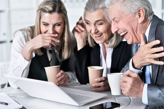 Three mature businesspeople using laptop while sitting at table