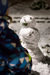 Child building a snowman at night. Kind baut Schneemann. in der Nacht