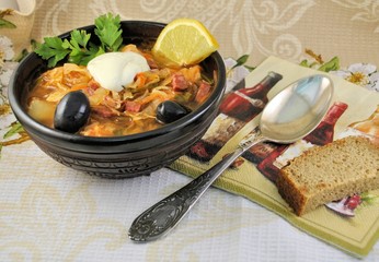 Red solyanka with white sour cream parsley and black olives cabbage ceramic plate bread silver spoon gray background