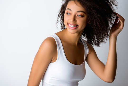 happy curly african american girl with dental braces, isolated on grey