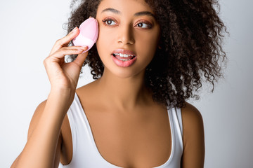 young african american woman using silicone cleansing facial brush, isolated on grey