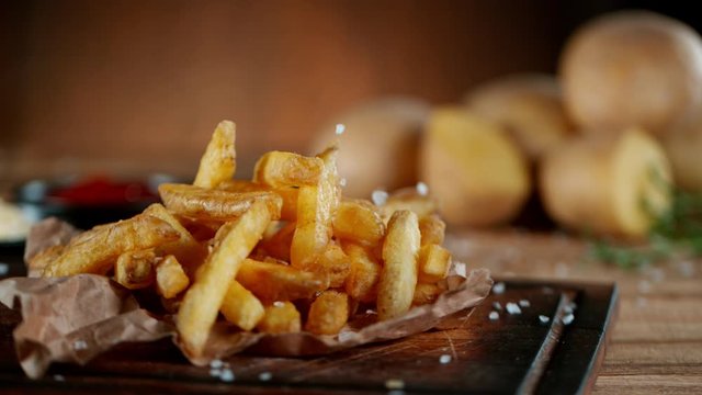 Super Slow Motion Shot of Falling Fresh French Fries on Wooden Table and Adding Salt at 1000fps.