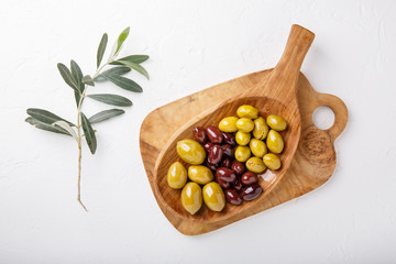 Different types of olives green and black on wooden plate on white table. Top view, copy space.