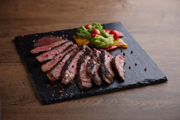 Appetizing and juicy meat steak with spices and a side dish on a stone plate on a wooden table.