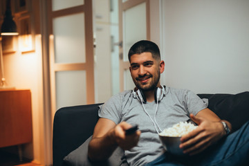 man at home watching tv and eating popcorn