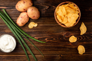 Crisps and green onion on dark wooden background.