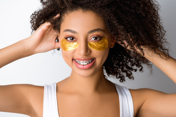 cheerful african american girl with golden eye patches and dental braces, isolated on grey