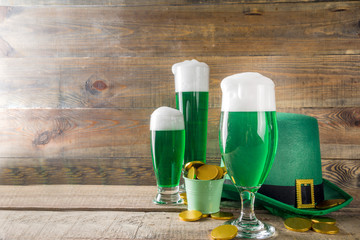 Traditional irish alcohol for St Patrick's day party. Different glasses with green beer, with golden chocolate coins decor and green leprechaun hat. Old rustic wooden background copy space