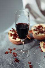 A wine glass with red wine stands on a gray grunge background next to grenades. Fruits and pomegranate wine on a concrete background