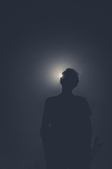 Silhouette of a person with sun behind causing sun eclipse effect. No colors. Dark and low angle image of someone unrecognizable.
