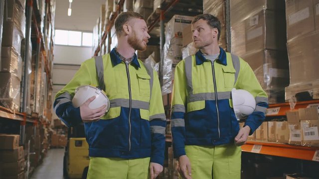 Two manual workers chatting during break in warehouse in front of racks
