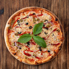 Top view of round pizza with red onion, black and green olives, melted cheese and ketchup on rustic textured background
