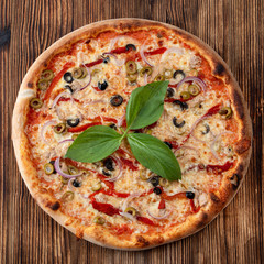 Top view of round pizza with red onion, black and green olives, melted cheese and ketchup on rustic textured background