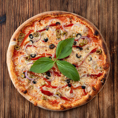 Top view of round pizza with red onion, black and green olives, melted cheese and ketchup on rustic textured background