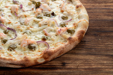 Italian seafood pizza with prawns and capers on rustic textured background