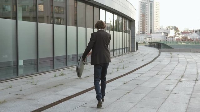 Businessman in a good mood after a working day. A man dances and crouches with happiness, listens to music through headphones.