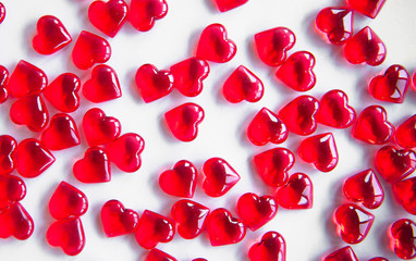 Festive background: many red hearts on a white background, lying in straight rows. Small stones in the shape of a heart